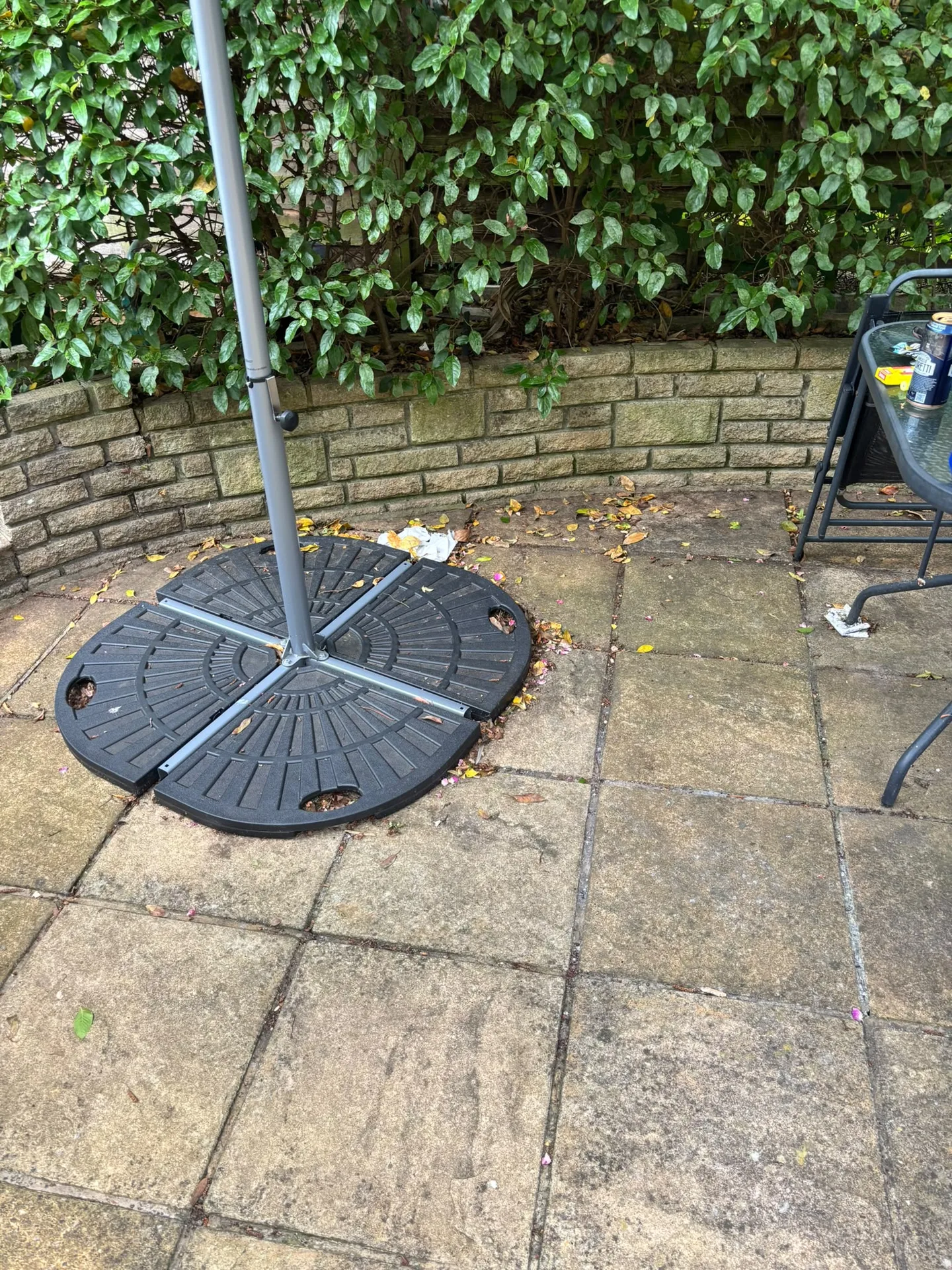 Grimy patio corner with parasol base and outdoor table before pressure washing in Woodford IG8 9JN