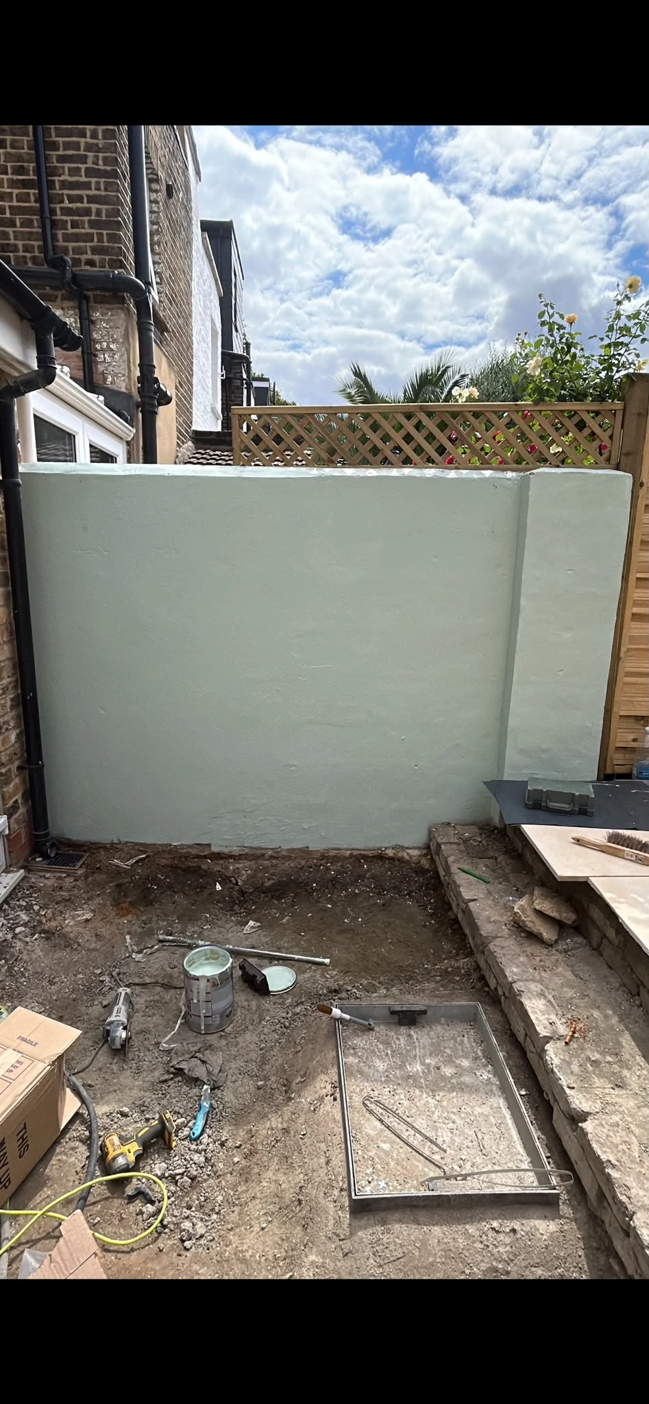 Greenwich garden mid-renovation showing the freshly rendered boundary wall, new trellis fitted on top and groundworks for the new porcelain patio and drainage